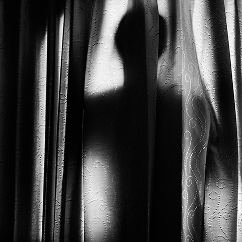 Machinal, a human shadow is cast on curtains in black and white