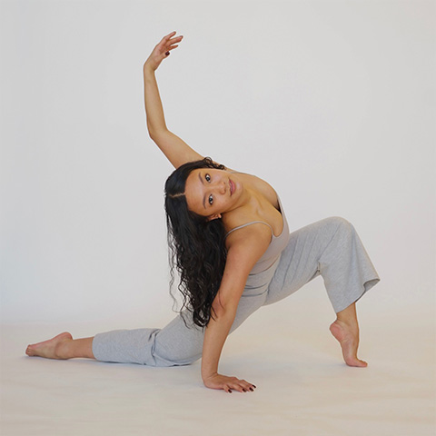 Kasey Aguilar posing with one arm up in the air with one leg bent up and one leg on floor