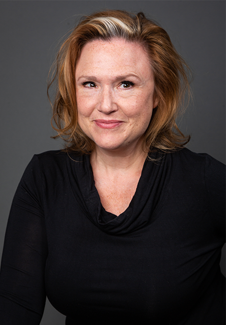 Jennie Israel headshot: smiling and wearing a v-cut long sleeve black top.