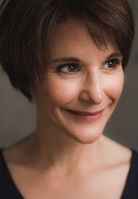 Wanda Strukus headshot: smiling with grey background wihle wearing a black u-length top.
