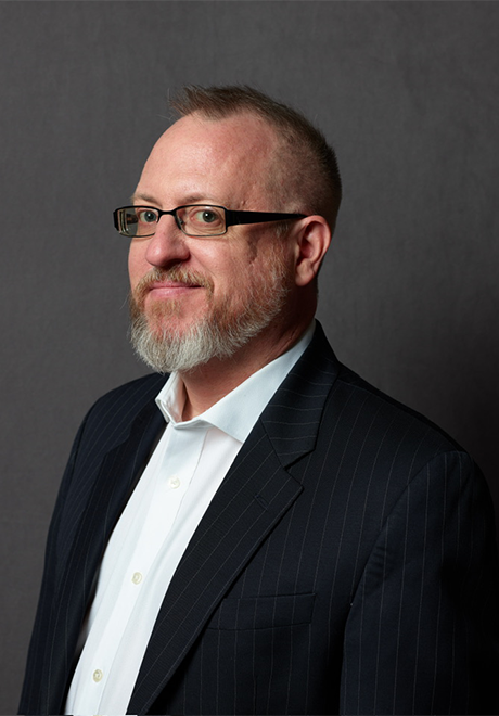 Andrew Bisantz smiling; wearing glasses in a black suit with a white undershirt