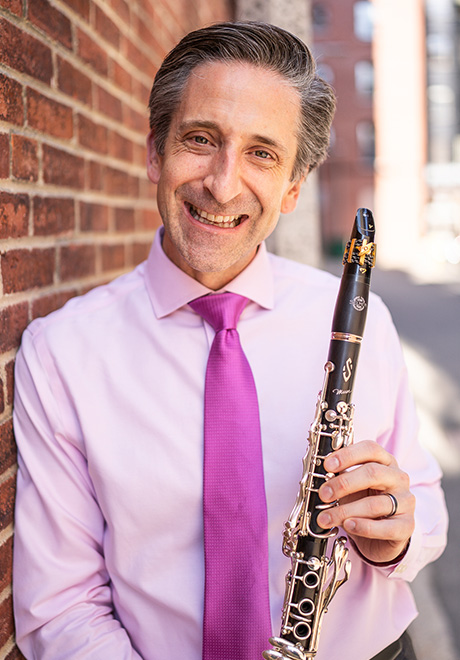 Matthew Marsit headshot, in pink shirt, pink tie, and holding clarinet.