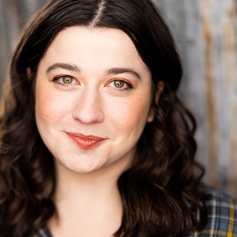 Katie Daye headshot: grinning in front of gray wall