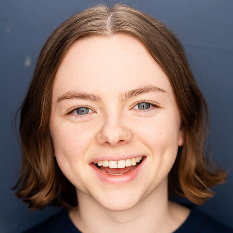 Bridget Delaney headshot: smiling in front of blue wall