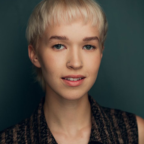 Eli Douglas headshot: in black top in front of dark teal wall