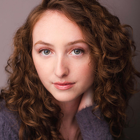 Haley Dunning headshot: wearing grey/purple sweater in front of medium grey wall