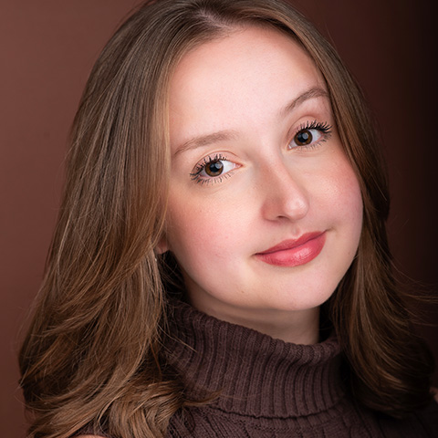Madeline Finkelman headshot: grinning in front of maroon wall