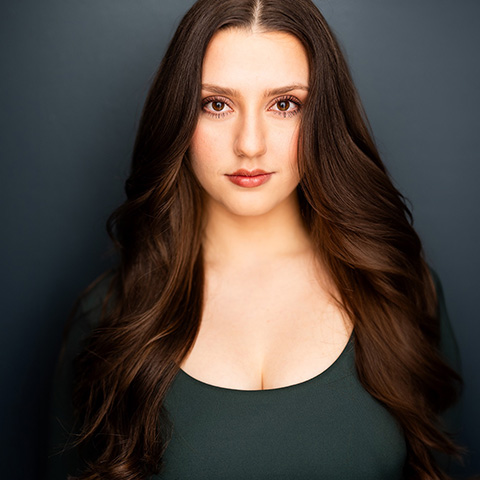 Annabella Hunt headshot: wearing teal/blue shirt in front of dark navy background