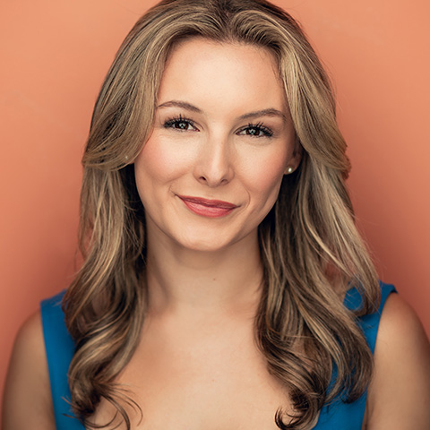 Haley Herman headshot: smiling in blue top in front of peach background