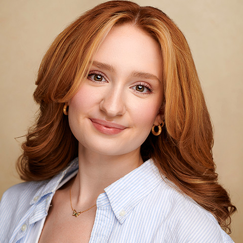McKenna Howell headshot: in white button up in front of beige wall