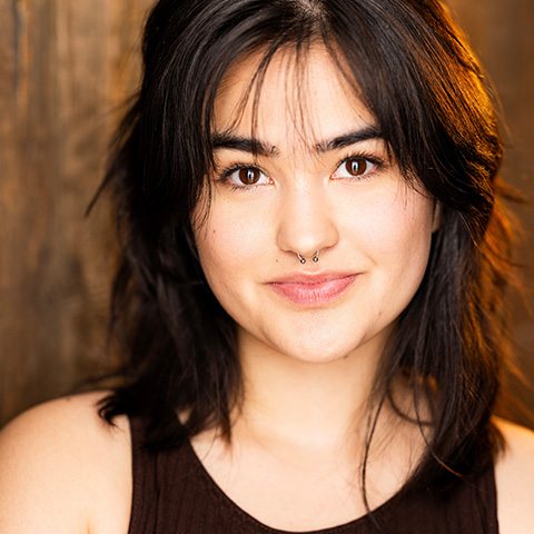 Melia Jost headshot: wearing black top in front of brown wall