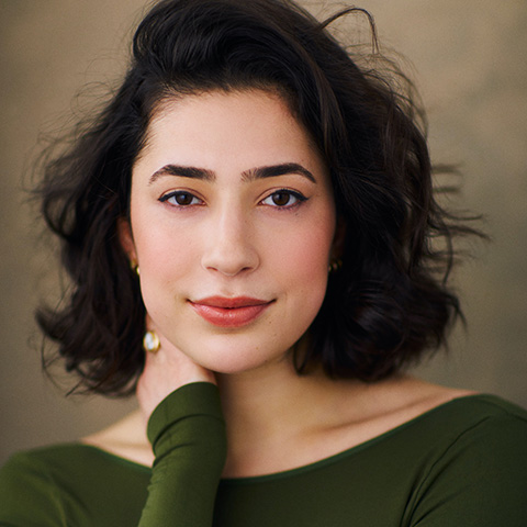 Hannah katz headshot: grinning in green shirt in front of brown background
