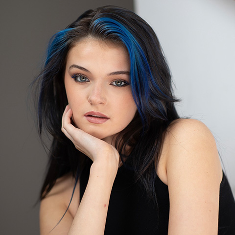 Heather Kirschner headshot: wearing black top in front of half gray half white hall