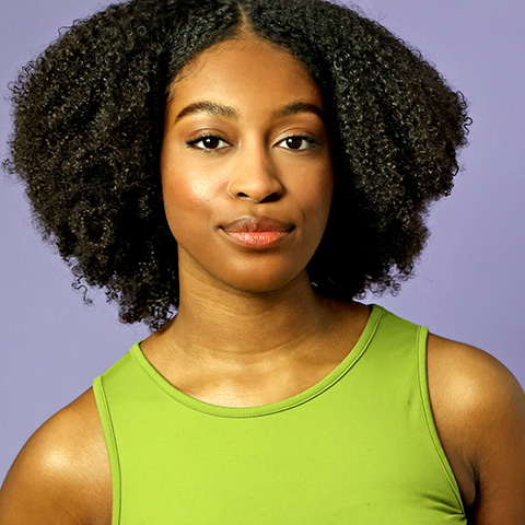 Rory Shirley headshot: wearing green top in front of purple background