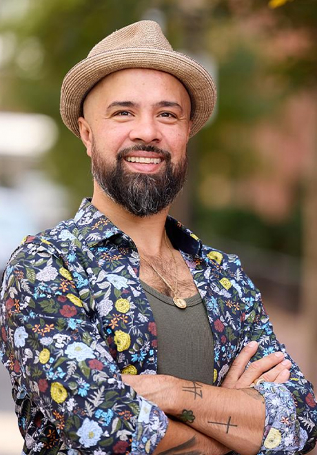 Nino De Los Reyes headshot: wearing a tan hat smiling with arms crossed