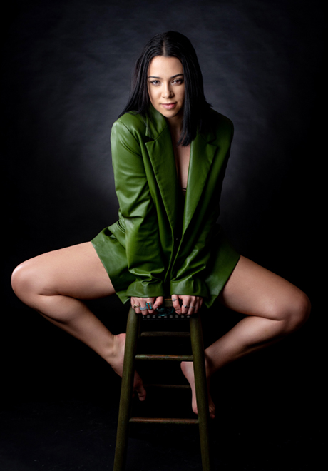 Alexis Beffer posing on a stool, wearing a green blazer.