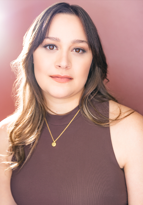 Holly Bourdon Faust headshot: grinning in front of a pale magenta wall in a mauve shirt.