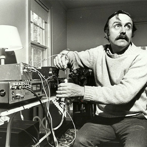 Black and white image of a man looking upwards while his hands are on a Sony synth board with wires.