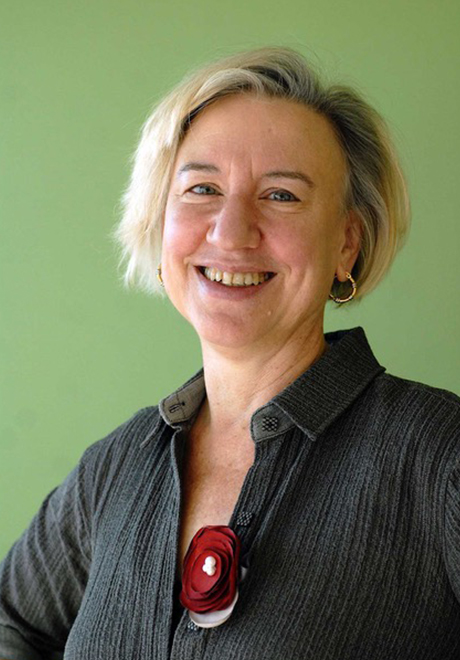 Aline Newton headshot: smiling in gray shirt in front of a green wall.