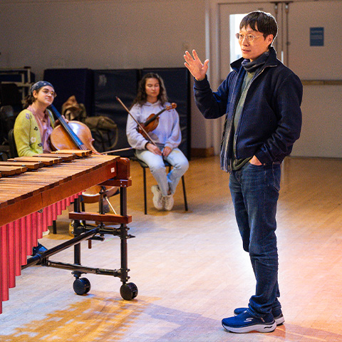 Lei Liang speaking with Boston Conservatory students. Liang is standing infront of a marimba.
