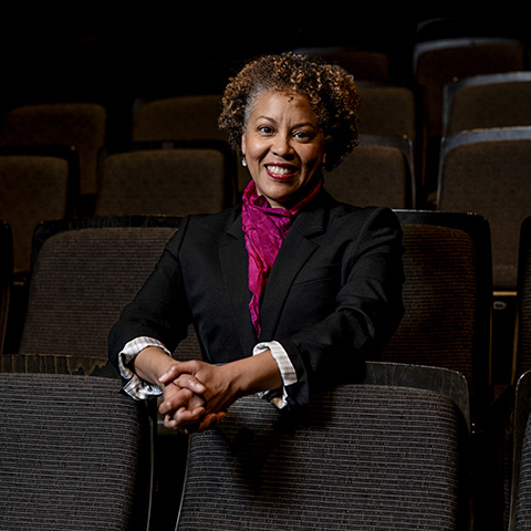 Krisha Marcano headshot: sitting in an auditorium with her hands together, leaning on the seat in front of her.
