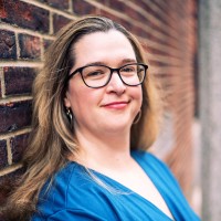 Hanna Oravec smiling in front of a brick wall in a blue shirt.