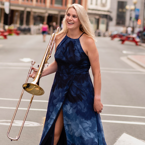 Hillary Simms in navy dress holding her trombone in the street