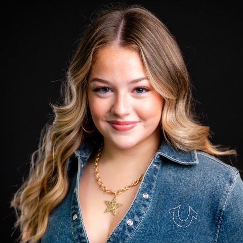 Cara Gonzales headshot: smiling in a denim jacket in front of a black background