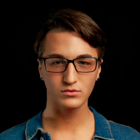 Marty Cardine headshot: Wearing glasses and a denim shirt in front of a black background