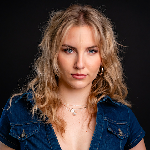 Evelyn Shymanski headshot: wearing denim shirt in front of a black background