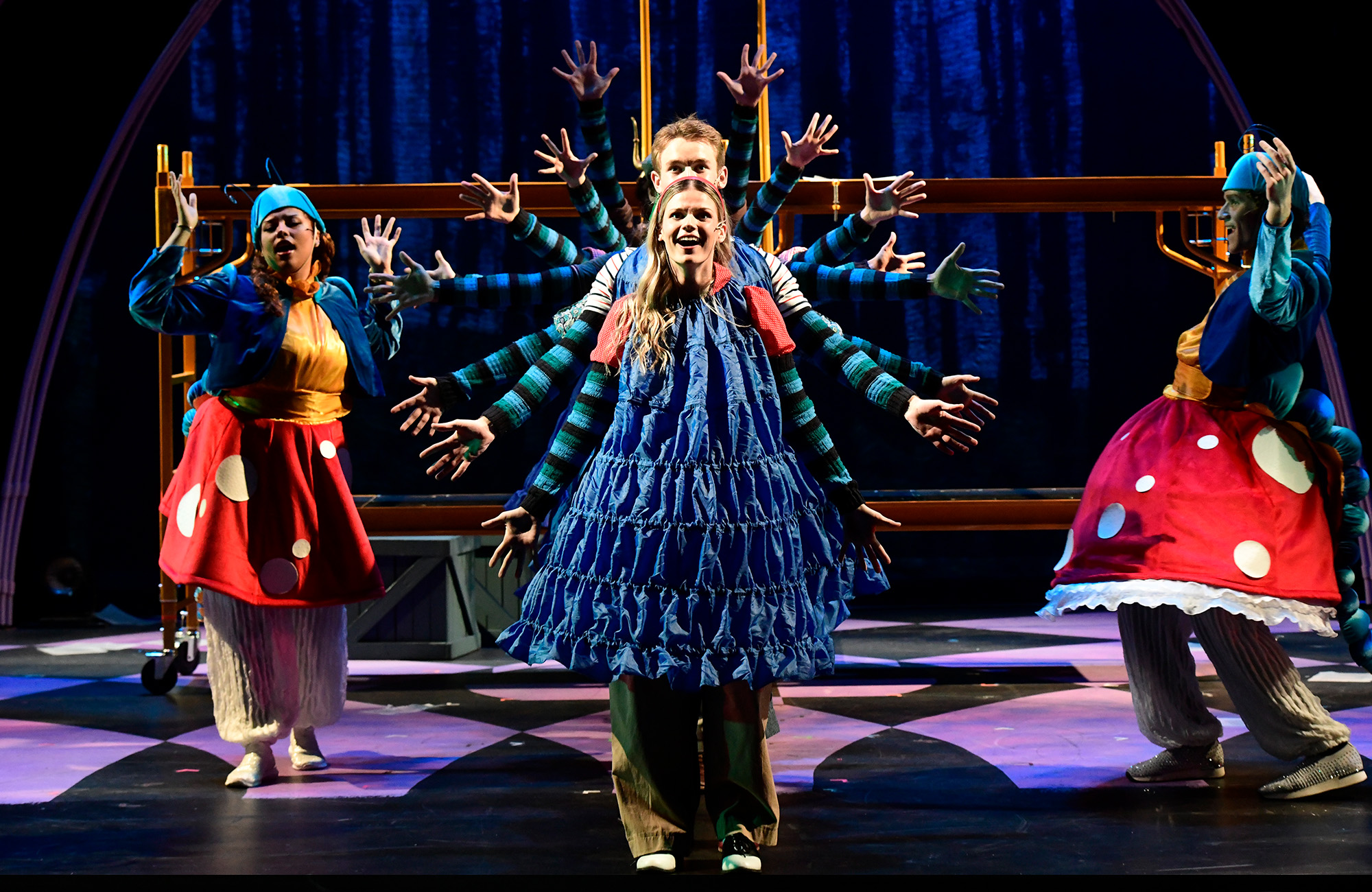 Theater students performing on stage in 'Alice by Heart' in a row with their arms spread out making a circle of arms