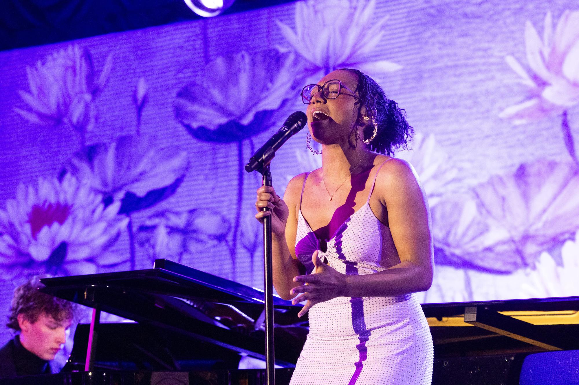 Student singing into a microphone on stage in a light purple dress