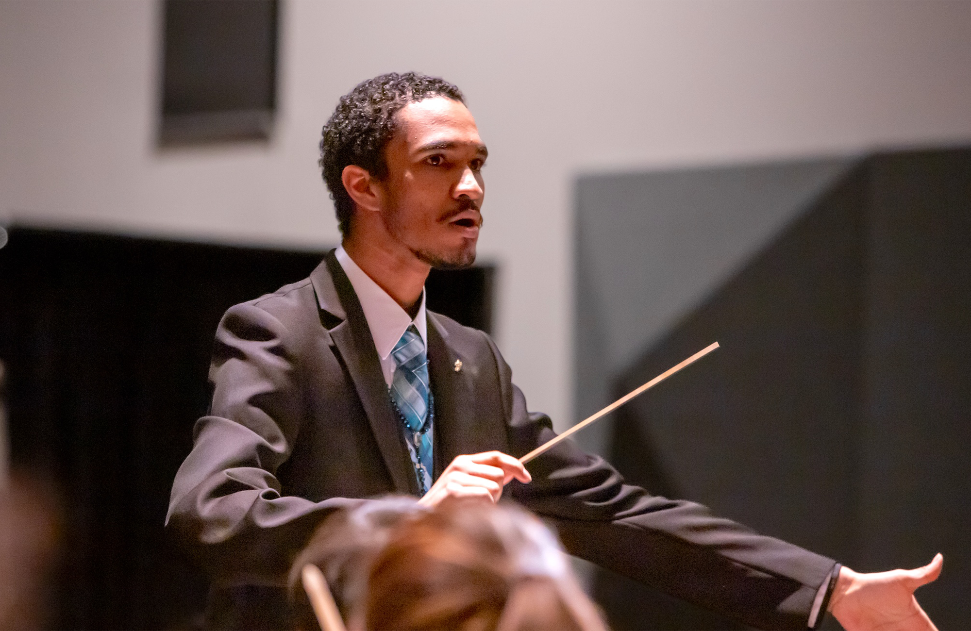 Conductor/percussionist Harold Rivas conducting an ensemble in a suit