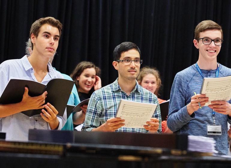 three singers look to the conductor holding music