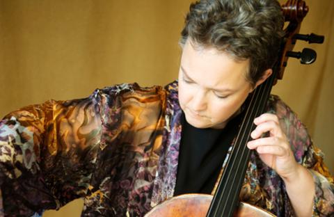 Rhonda Rider looking down playing the cello with a tan background