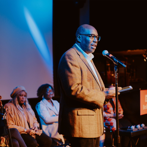 Chair Mike Mason speaking at a podium, on stage with students.