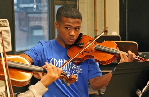 Student is wearing a blue t-shirt playing the violin.